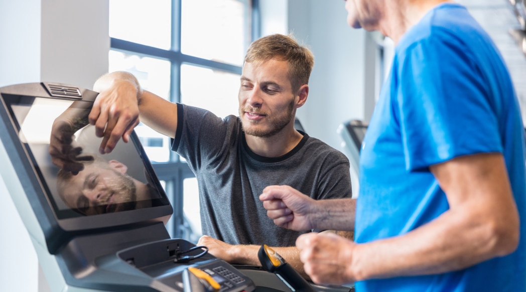 A trainer helps instruct a patient on a treadmill.