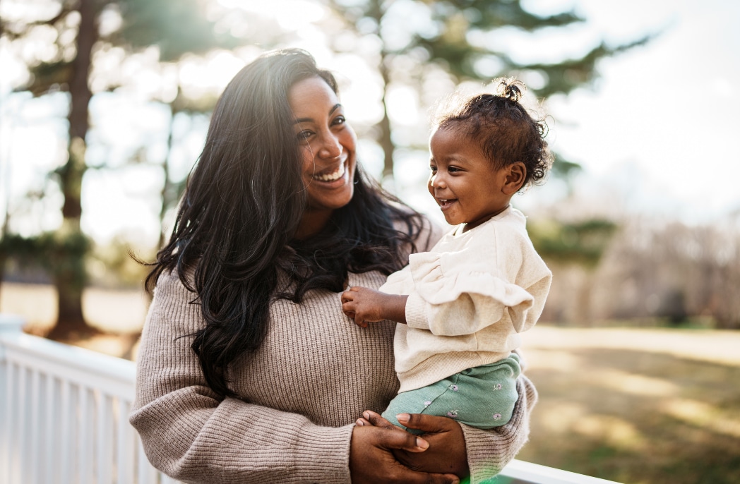 A mother holds her daughter on their front porch, both smiling.