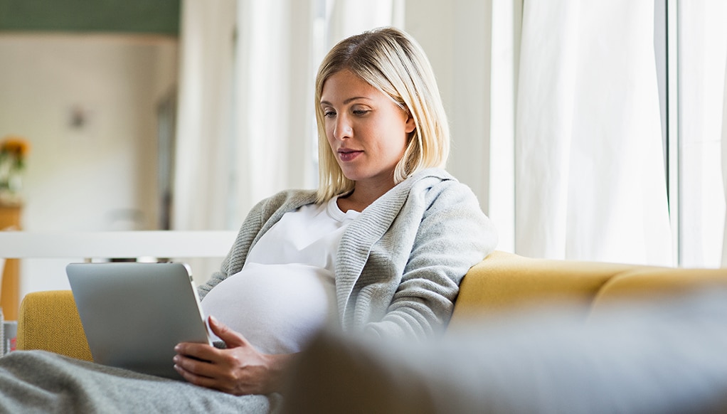 Full term pregnancy young woman on sofa using digital tablet