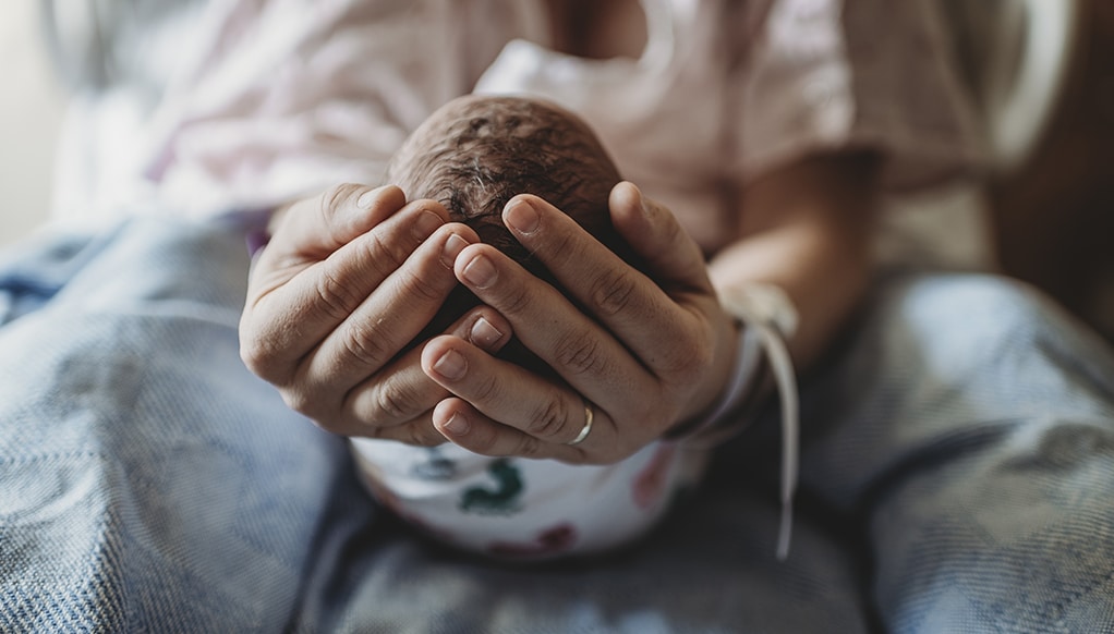 Macro view of mothers hands holding newborn boy's head