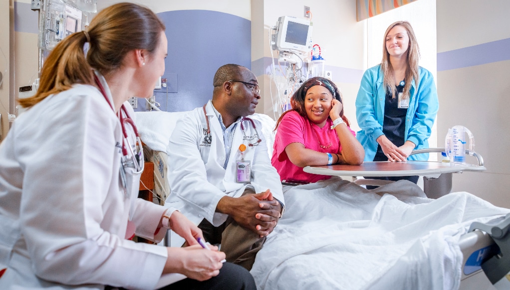 Maynard Children's Hospital care team members sit on with a patient and talk to one another.