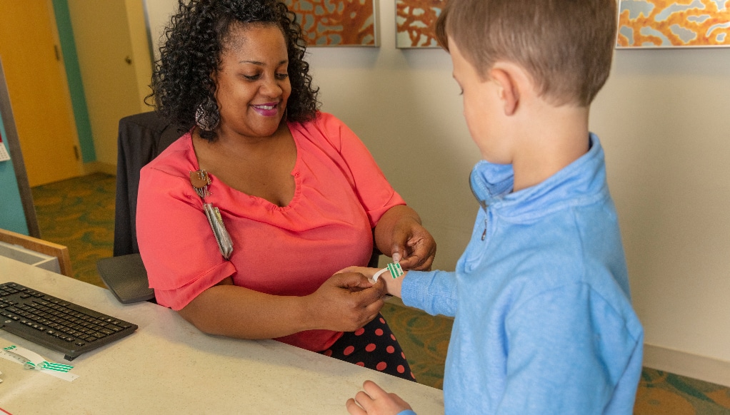 A Maynard Children's Hospital team member puts a bracelet on a young patient while they both smile.