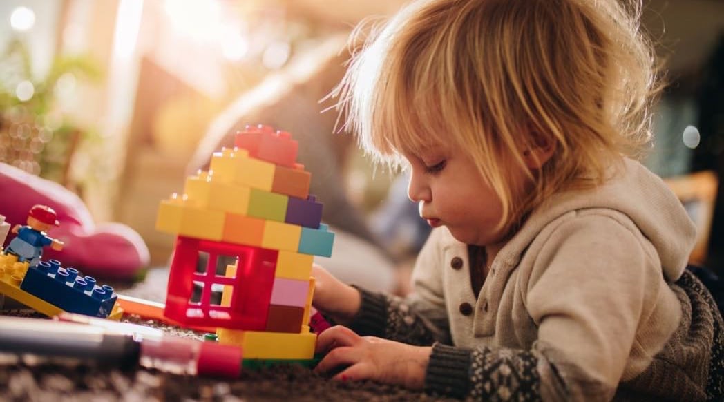 Small boy playing with plastic blocks on the floor.