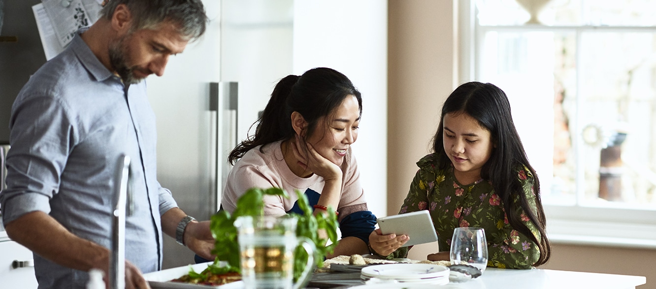 Mother and daughter looking at tablet while father prepares home made meal