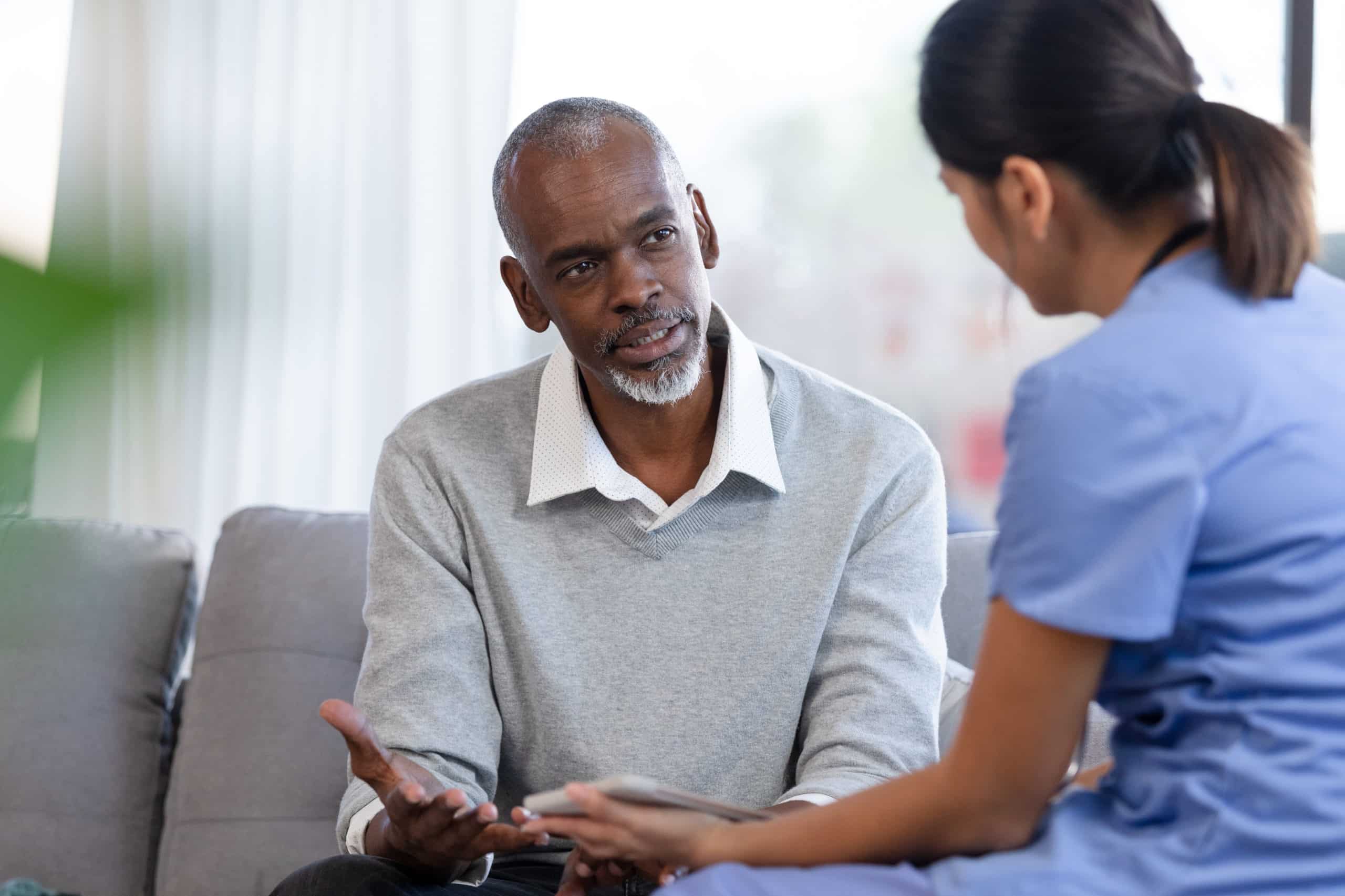 Senior man gestures while speaking with nurse A man discusses symptoms with a nurse