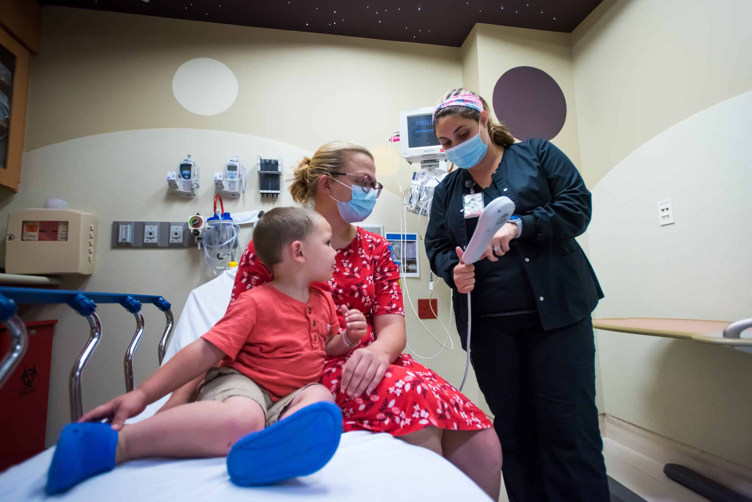 A nurse helps a mother and a pediatric patient settle into their room.
