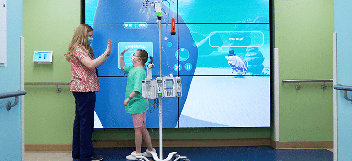 A patient celebrates with a team member after completing a task on the PICU interactive wall.