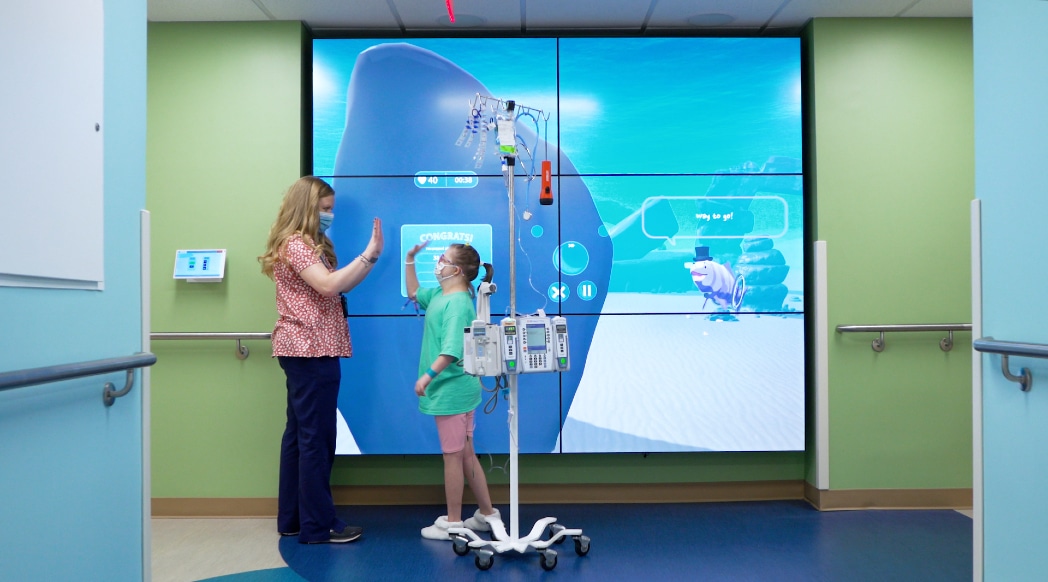 A team member and pediatric patient celebrate in front of the interactive wall at the Maynard Children's Hospital at ECU Health Medical Center.