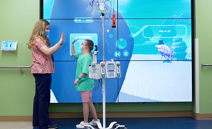 A pediatric patient and a child life specialist play with the interactive wall at the James and Connie Maynard Children's Hospital.
