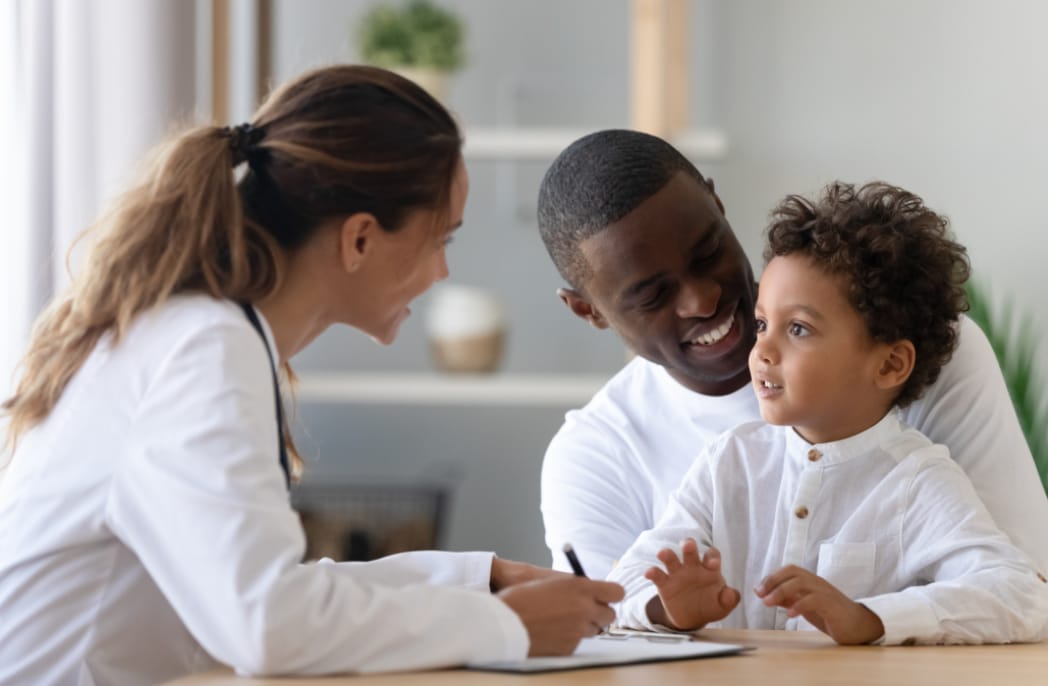 A health care provider speaks to a pediatric patient and their father.