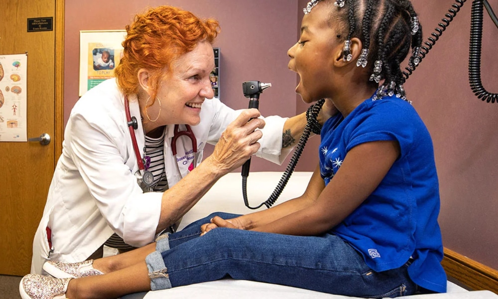 A provider examines a pediatric patient who sits on the exam table.