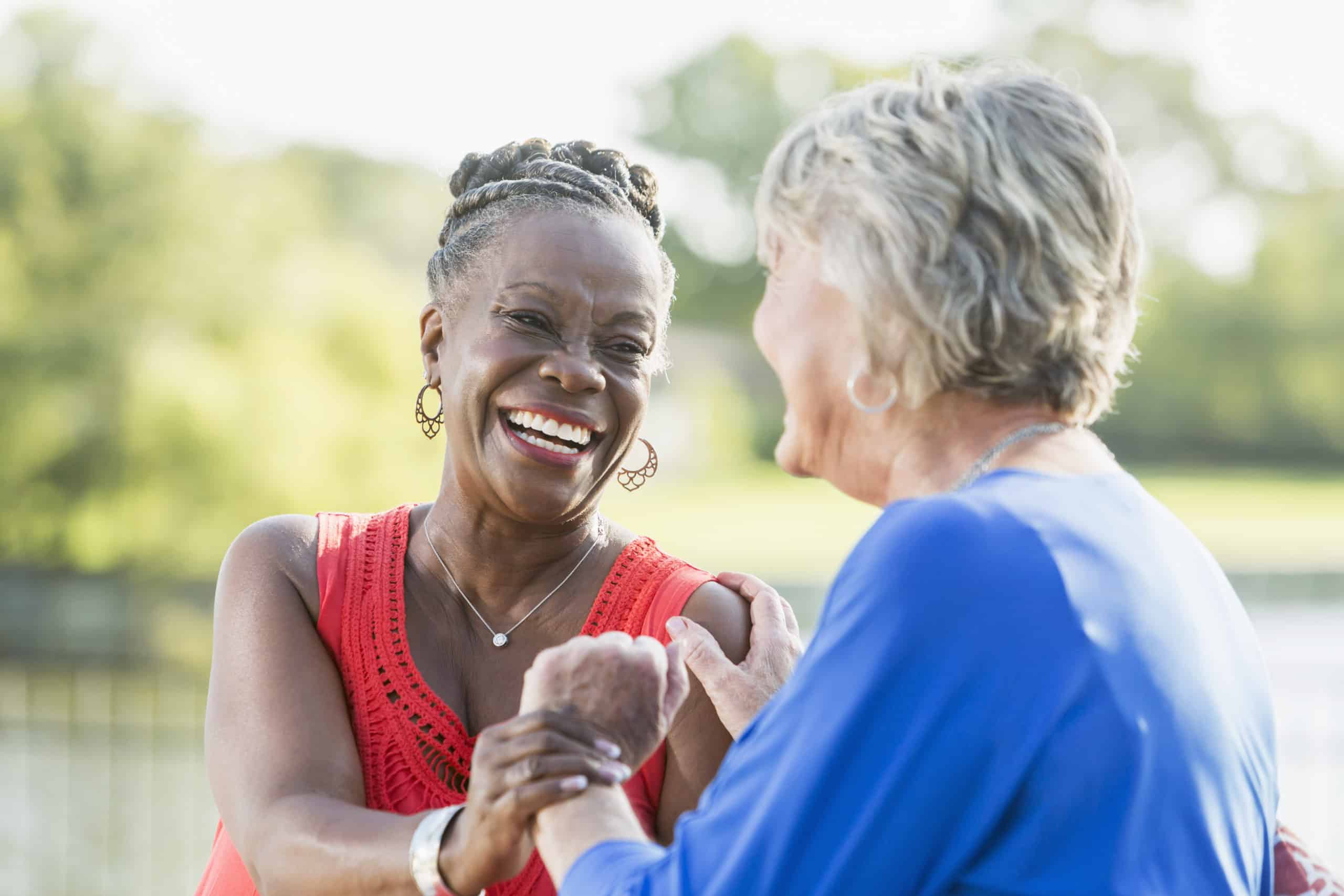 Senior multi-racial women, best friends, laughing Two senior multi-ethnic woman, one Caucasian and the other African American, sitting in back yard by water enjoying each other's company. They are looking at each other, laughing.