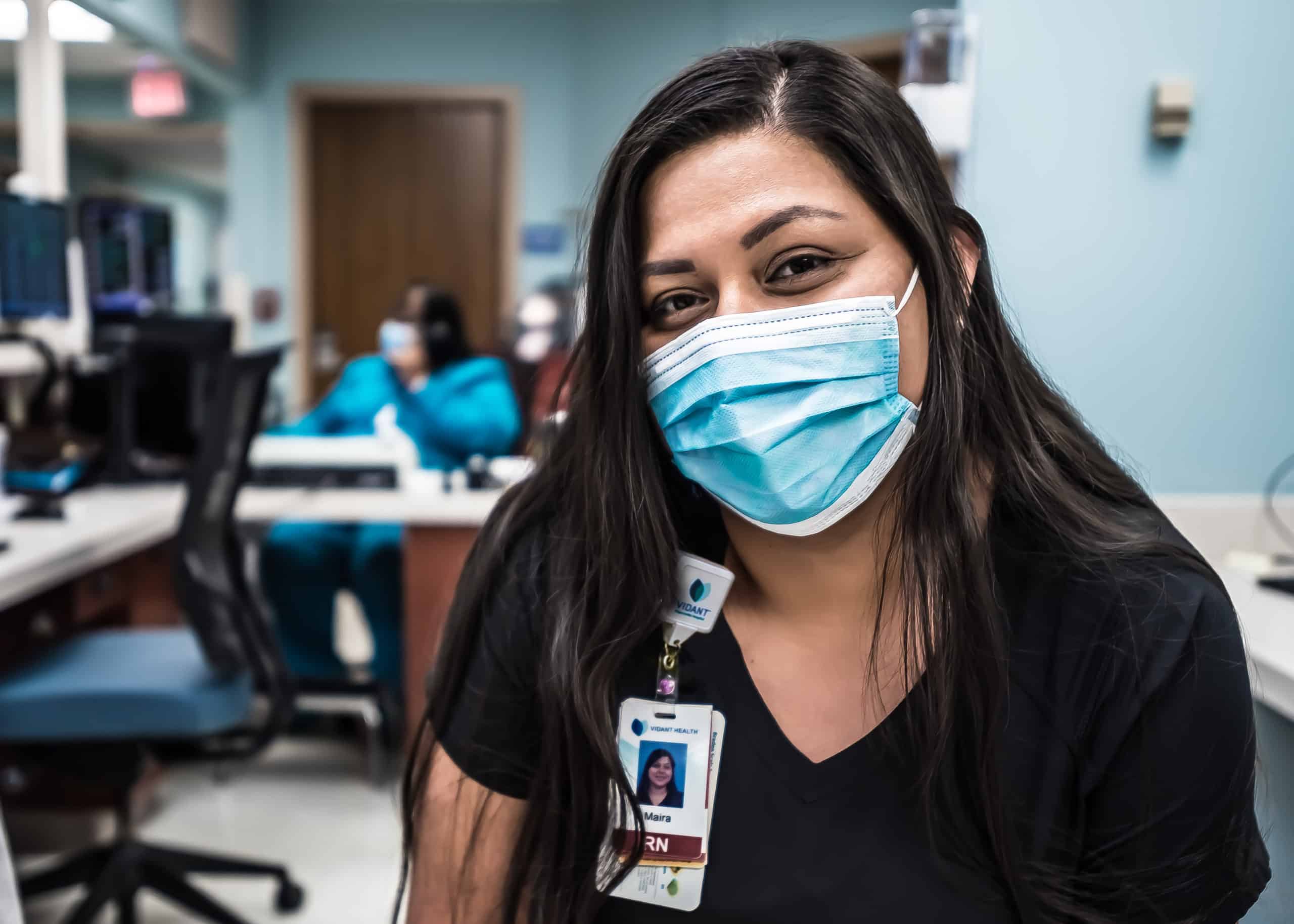 ECU Health nurse Maira Sanchez smiles under her mask at a nurses station at ECU Health Medical Center.