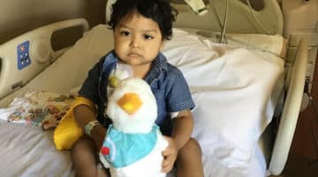 Pediatric patient Miguel Morales sits in a hospital bed with a stuffed animal.