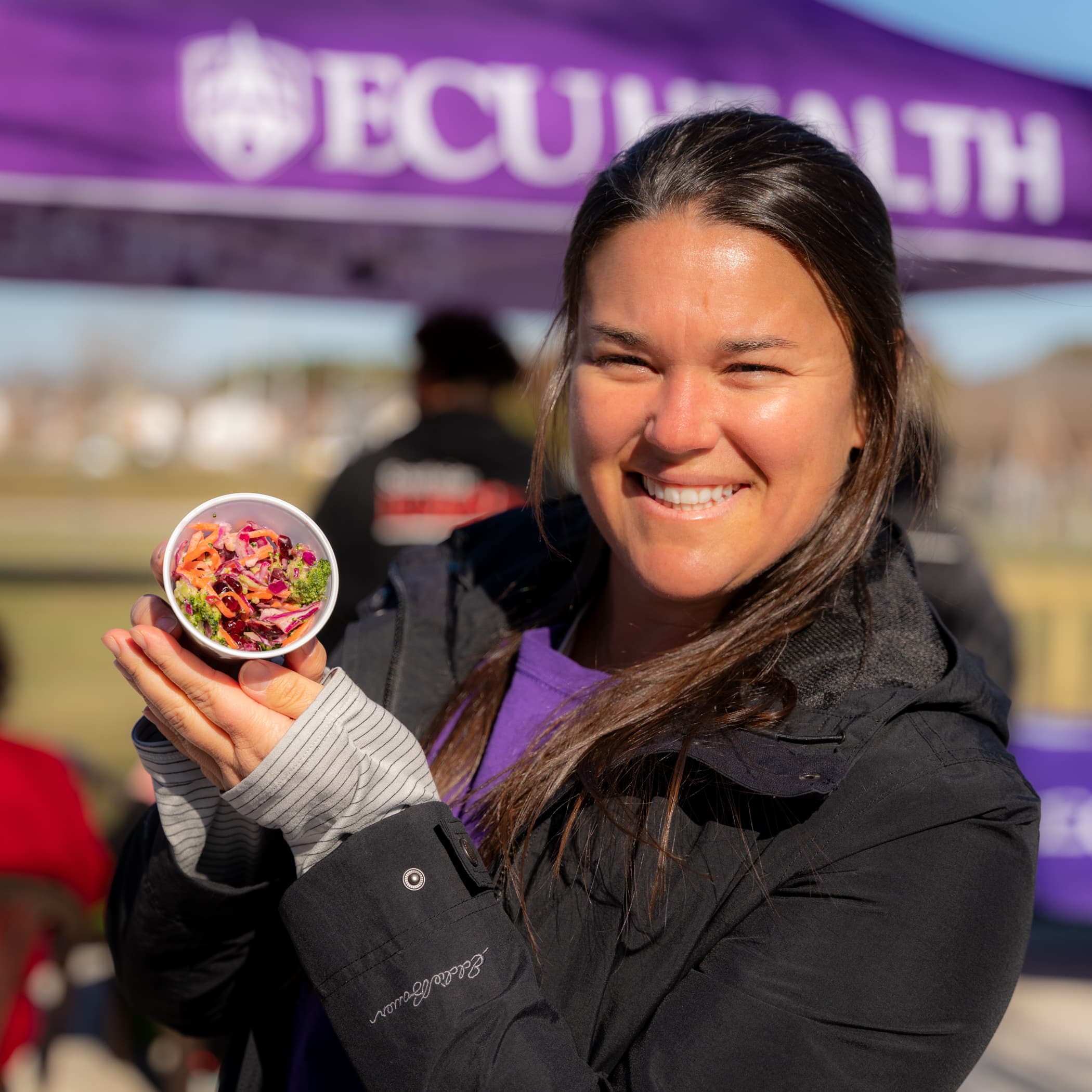An ECU Health nutritionist holds up a sample of a kale salad recipe that the team was sharing with community members at the Beaufort Community Garden outside of the ECU Health Wellness Center - Washington.