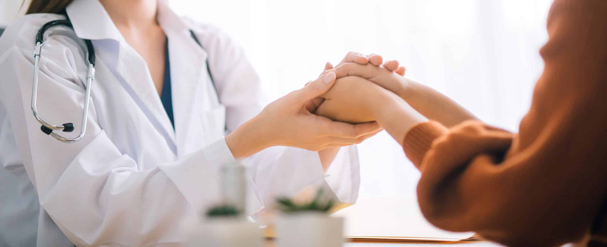 A provider holds her patient's hand to reassure her.