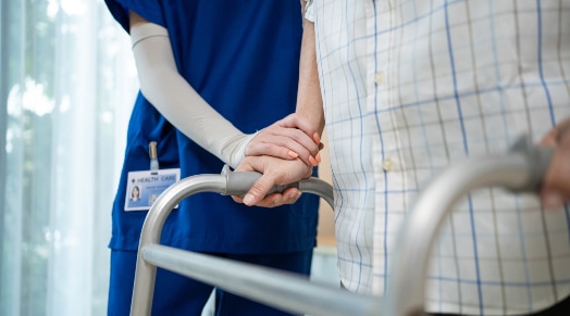 A nurse helps a patient using a walker.