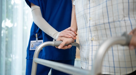 Acute Rehab 1 A nurse helps a patient using a walker.