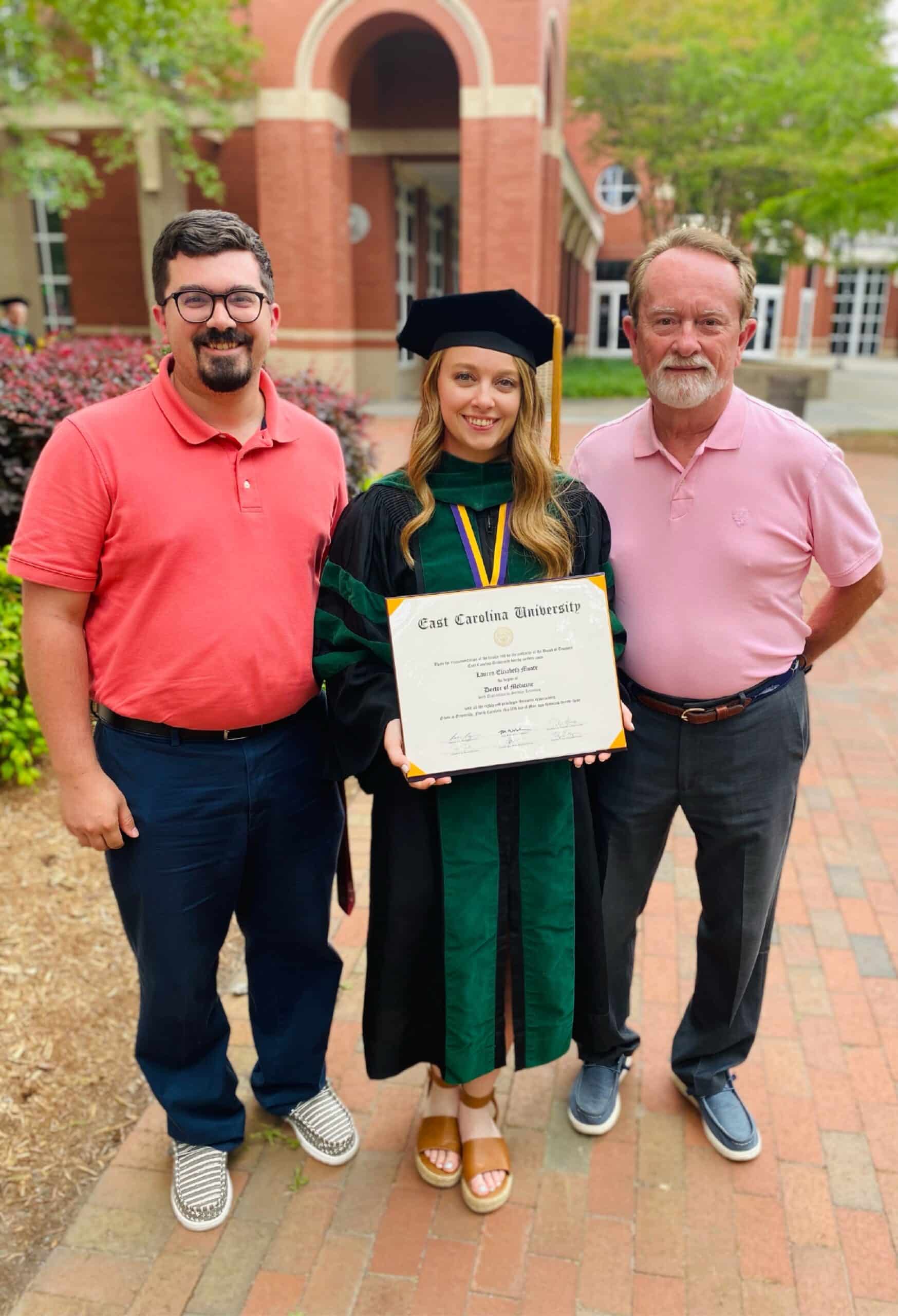 Lauren Moore poses for a photo with her family following her graduation ceremony at the Brody School of Medicine at East Carolina University. Lauren wears her cap and gown while holding her diploma in front of her.