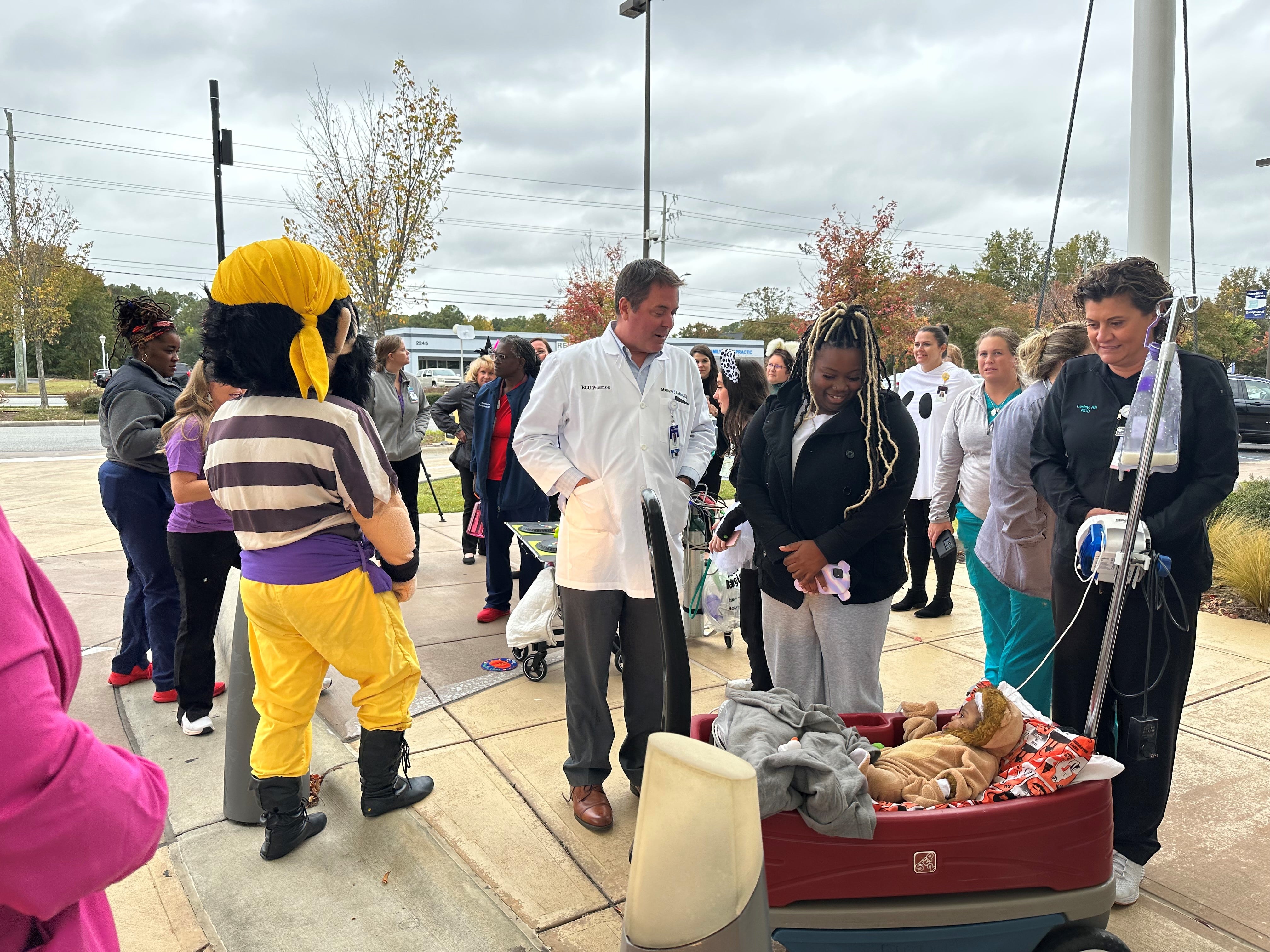 Dr. Matthew Ledoux speaks to the parent of a patient, who is riding in a red wagon and wearing a lion costume while attending the Maynard Children's Hospital Halloween parade.