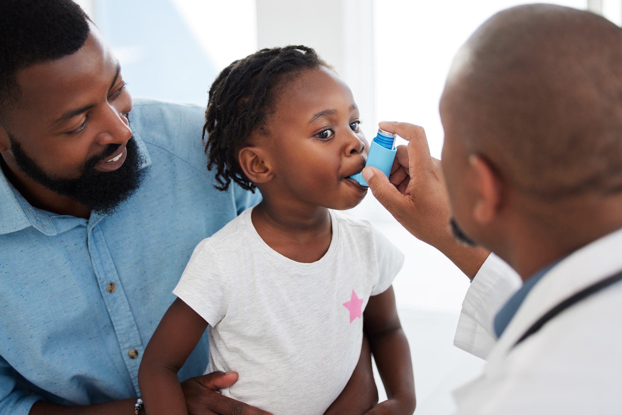 Doctor helping a child patient with an inhaler for asthma in his office at a medical clinic. Healthcare worker consulting a girl with chest or respiratory problems with pump in a children's hospital.