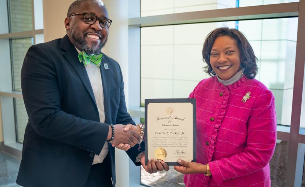 Chad Tucker, director of the Volunteer Services Department at the Medical Center, shakes hands with Jennifer Congleton, administrator of pastoral care and volunteer services, while they hold the North Carolina Governor’s Award for Volunteer Service: Paid Volunteer Director.