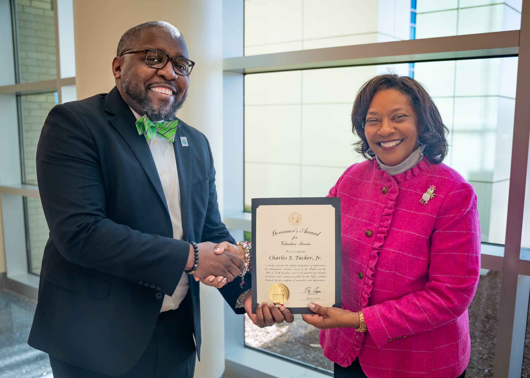 Chad Tucker, director of the Volunteer Services Department at the Medical Center, shakes hands with Jennifer Congleton, administrator of pastoral care and volunteer services, while they hold the North Carolina Governor’s Award for Volunteer Service: Paid Volunteer Director.