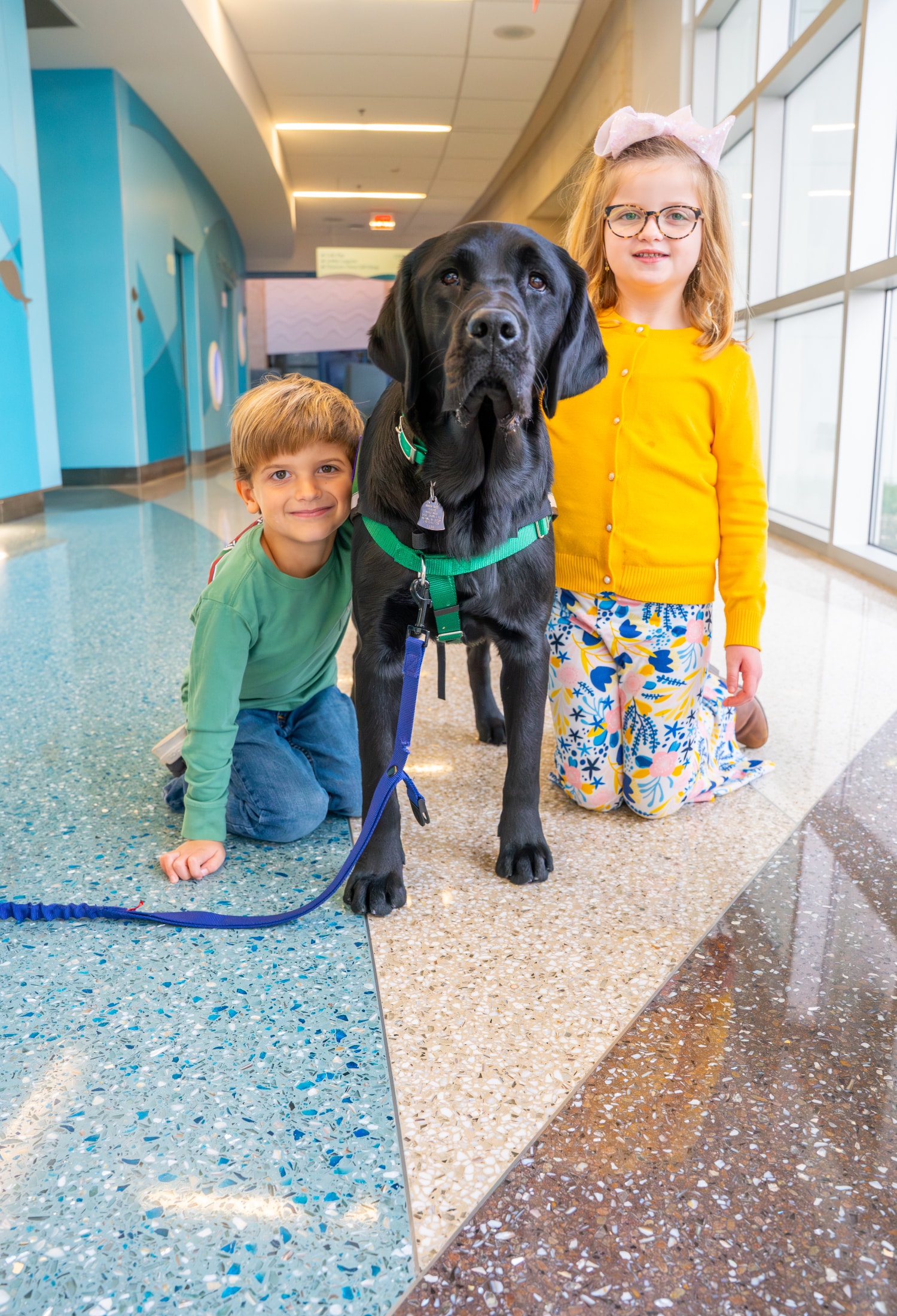 Two visitors to Maynard Children's Hospital kneel next to Maynard Canine Crew's pup, Sam.
