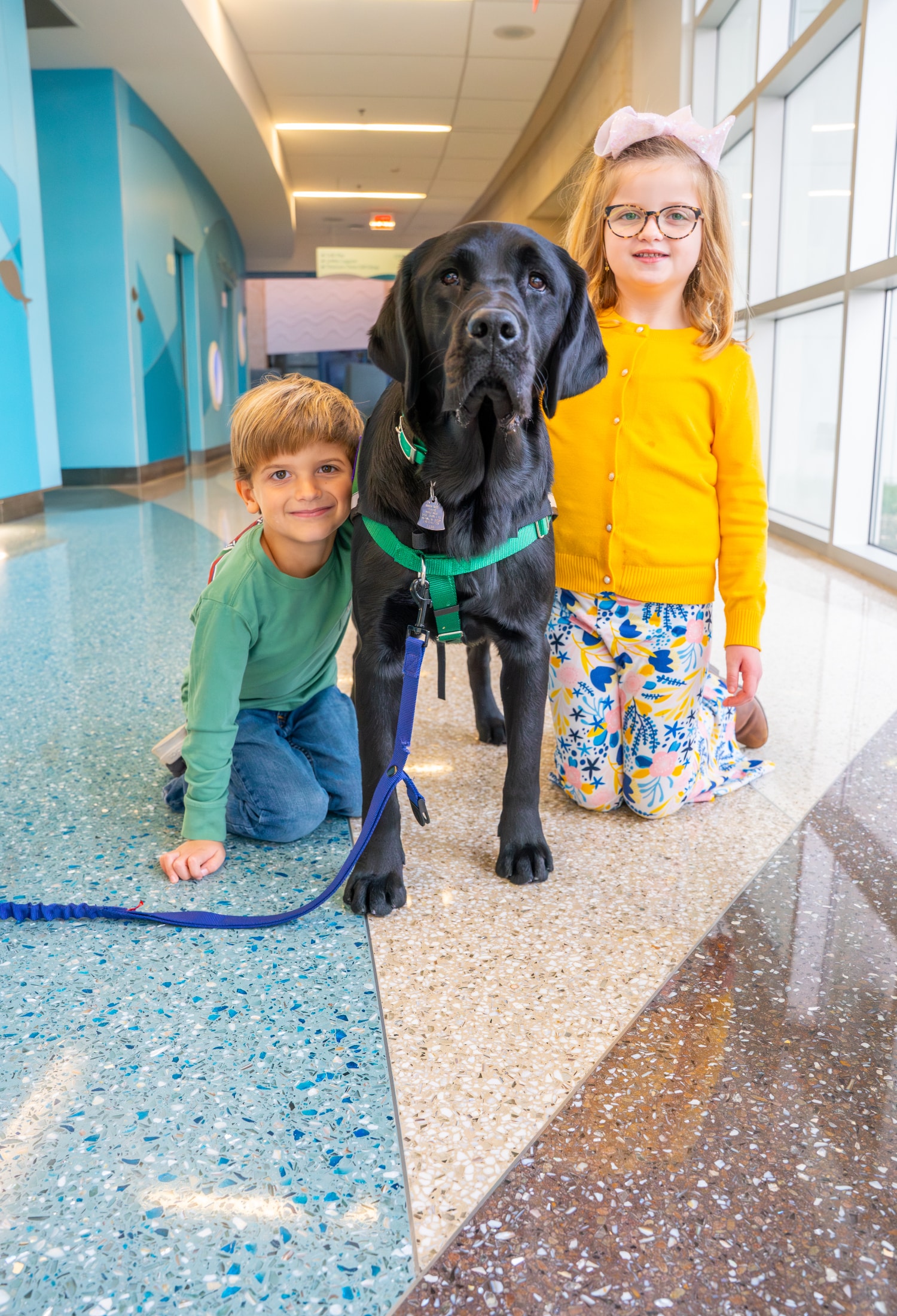 MCH-CanineCrew-Sam-1860 Two visitors to Maynard Children's Hospital kneel next to Maynard Canine Crew's pup, Sam.