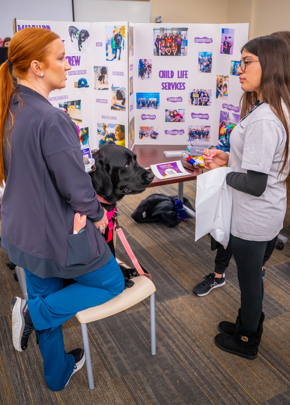 A student speaks with a Maynard Canine Crew handler, along with the crew's dog Sam, during the Health Sciences Academy career fair on March 5, 2024.