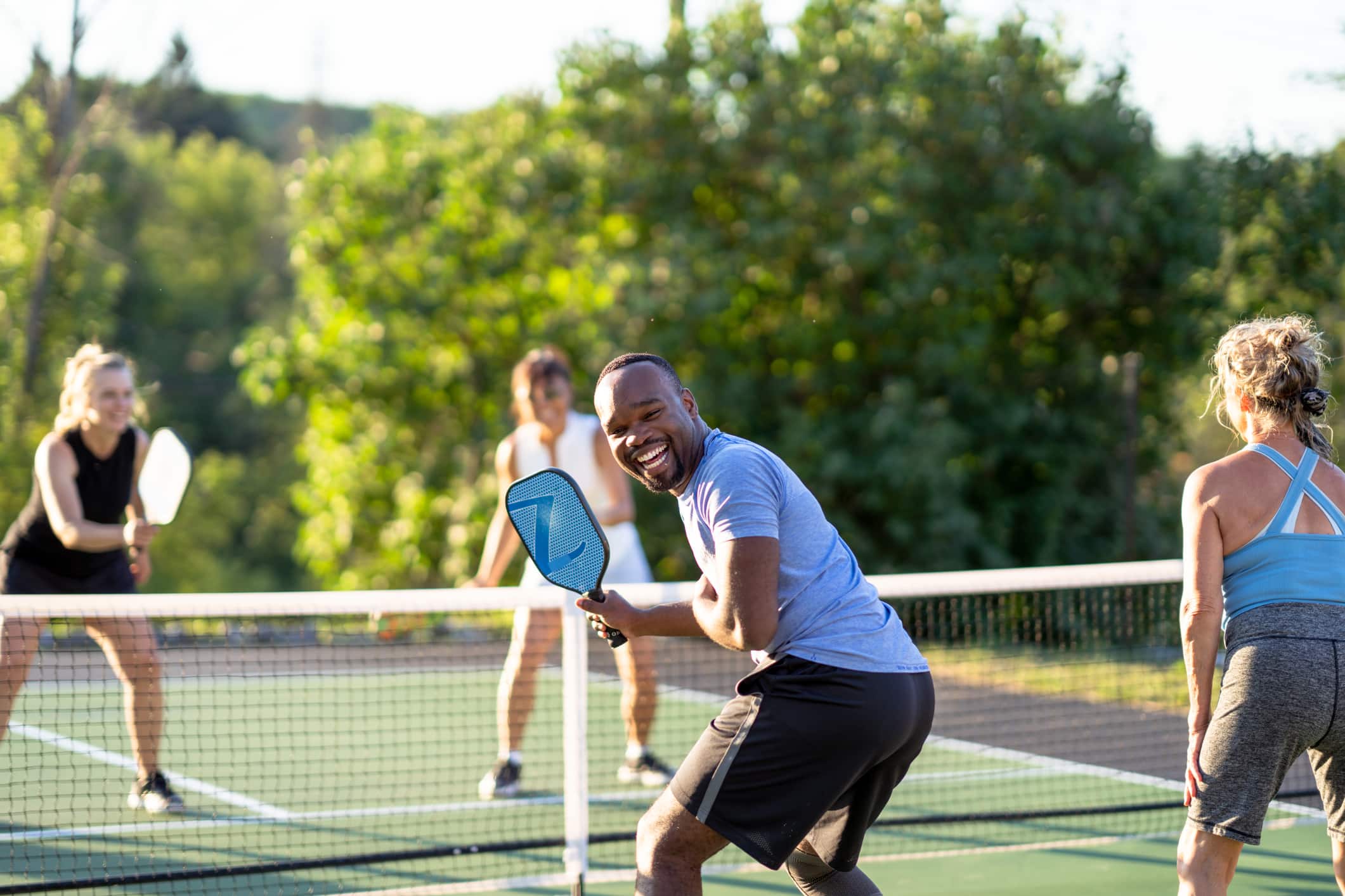 A group of friends plays pickleball together on an outdoor court on a sunny day.