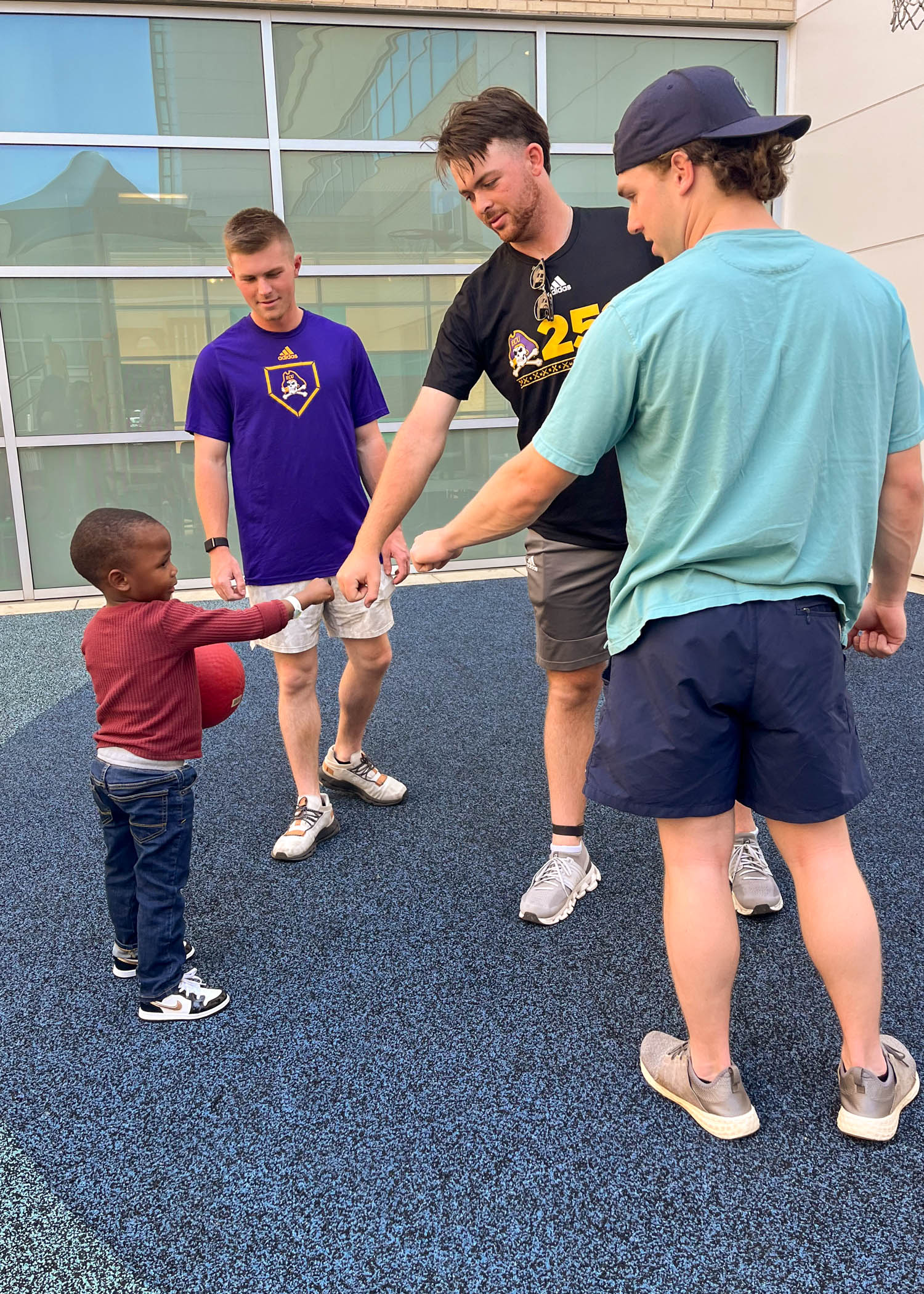 ECU baseball players Joey Berini, Jake Hunter and Nathan Chrismon play with a pediatric patient at the Maynard Children's Hospital playground.