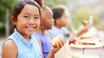 A young girl eats an apple during a lunch outside in the sun.