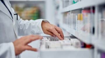 A pharmacist looks through medications in a drawer.