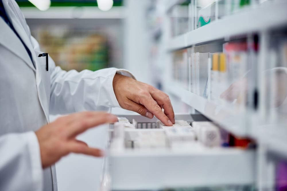 A pharmacist looks through medications in a drawer.