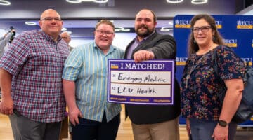 Cooper Butts holds a sign announcing his match at ECU Health and stands next to a sibling and his parents.