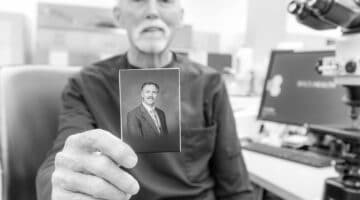 Berry Warren sits at his desk and holds a picture of himself during his early days at ECU Health.