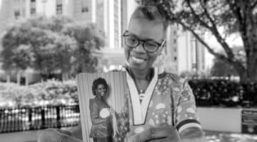 Valorie Nelso poses in front of ECU Health Medical Center with a photo of herself from early in her career.